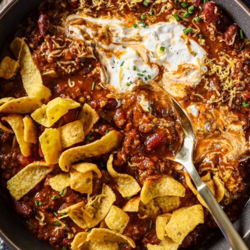 Slow cooker chili plated in gray bowl with friots, shredded cheese, and sour cream.