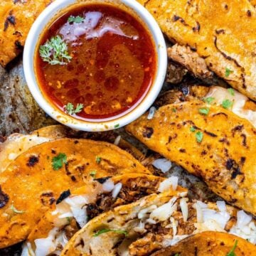 Close up of Birria Tacos with chopped onions, consume, and fresh cilantro