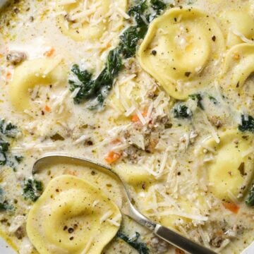 Close up of Creamy Sausage, Kale, Ravioli Soup topped with Parmesan in a white bowl.
