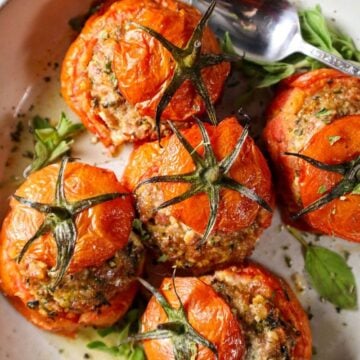 Roasted Sausage & Herb Stuffed Tomatoes on a white plate with fresh herbs.