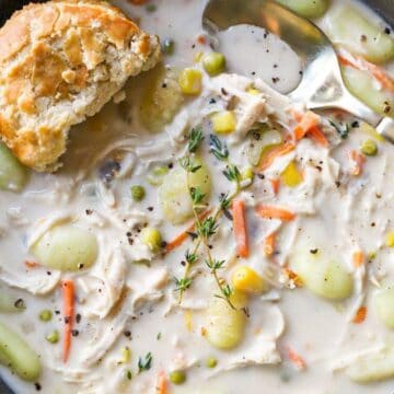 Chicken pot pie soup in a grey bowl with biscuits and a gold spoon.