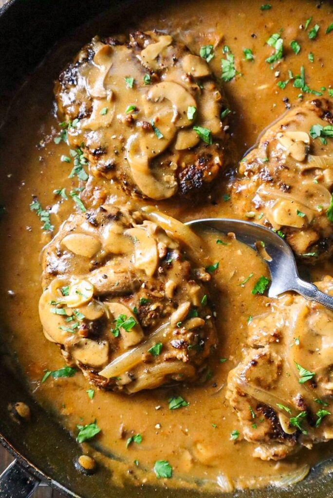 Salisbury steak in a frying pan with mushroom and shallot gravy.