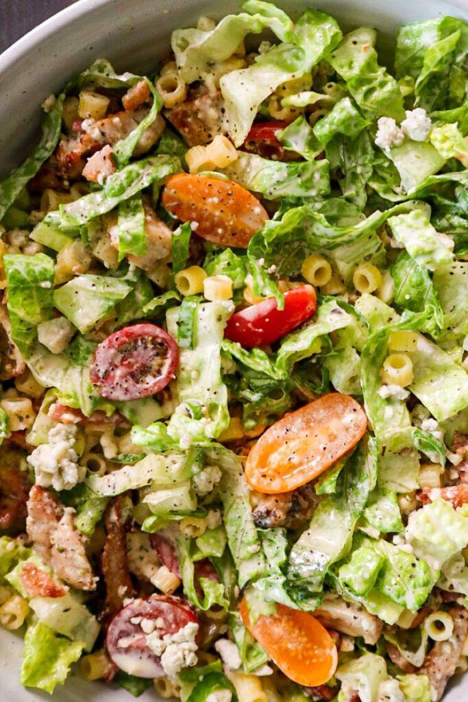 Close up of Portillos Chopped Salad with tomatoes, chicken, bacon, Gorgonzola cheese, and dressing in a white bowl. 