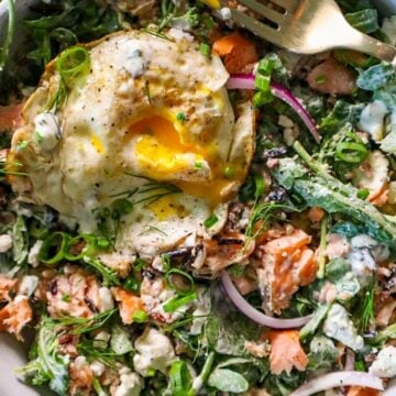 Hot smoked salmon, goat cheese, and avocado salad with creamy dill dressing and a fried egg in a white bowl.