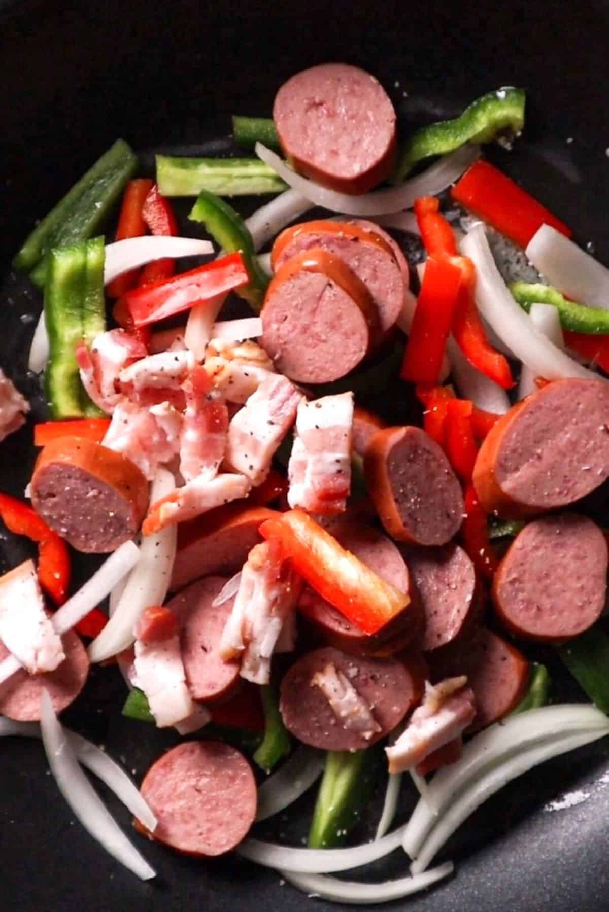 sausage onion peppers and bacon in frying pan